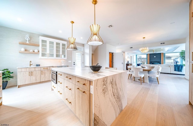 kitchen with light hardwood / wood-style flooring, hanging light fixtures, a center island, light stone counters, and light brown cabinets