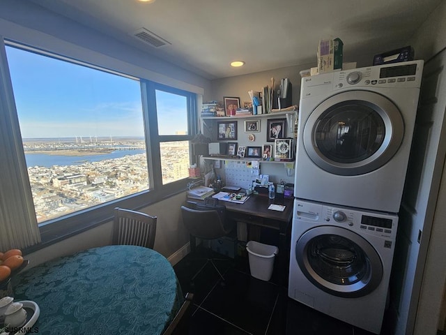 laundry room featuring a water view, stacked washer and dryer, and dark tile patterned floors