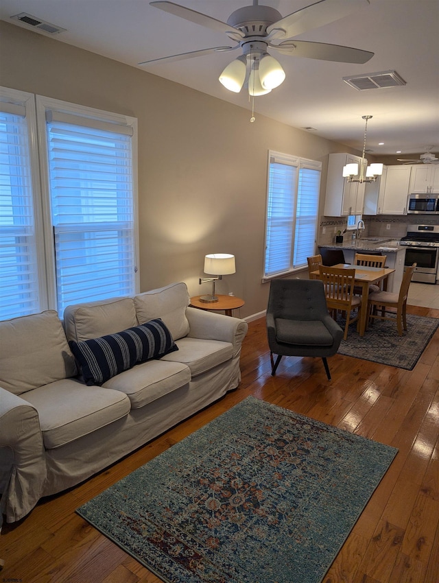 living room featuring hardwood / wood-style floors, ceiling fan with notable chandelier, and sink