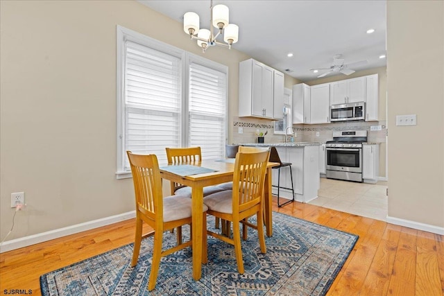 dining space with sink, ceiling fan with notable chandelier, and light hardwood / wood-style floors