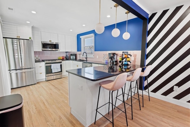 kitchen featuring a breakfast bar area, decorative light fixtures, appliances with stainless steel finishes, kitchen peninsula, and white cabinets