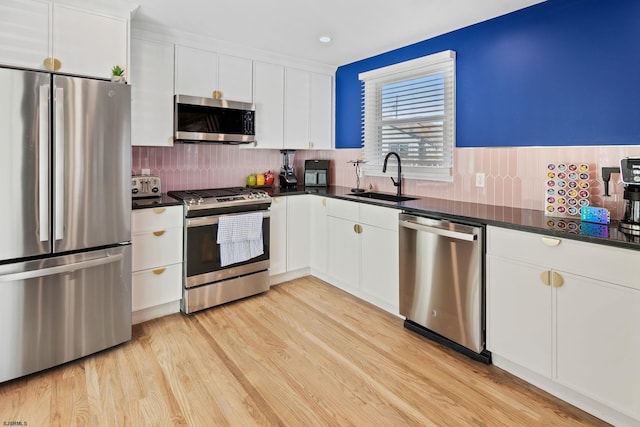 kitchen with sink, tasteful backsplash, light wood-type flooring, stainless steel appliances, and white cabinets