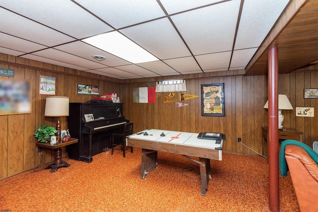 rec room with a paneled ceiling, carpet, and wood walls