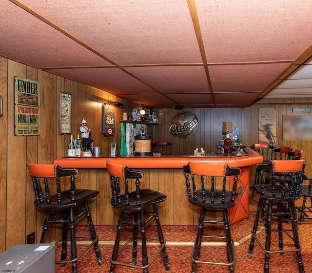 bar with a paneled ceiling, wooden walls, and carpet