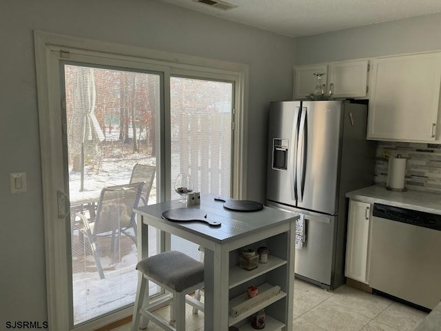 kitchen featuring stainless steel appliances, light tile patterned flooring, white cabinets, and decorative backsplash