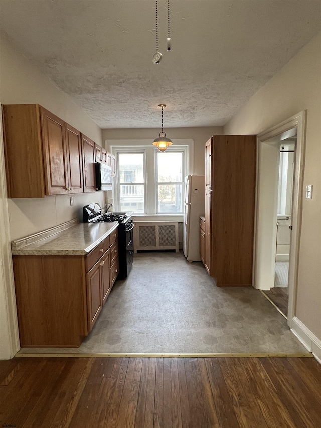 kitchen with black gas range oven, hanging light fixtures, hardwood / wood-style floors, and white fridge