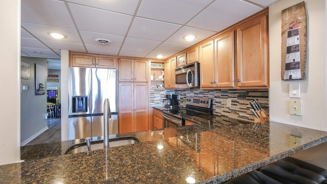 kitchen featuring sink, decorative backsplash, dark stone counters, kitchen peninsula, and stainless steel appliances