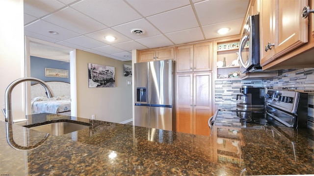 kitchen with appliances with stainless steel finishes, sink, backsplash, dark stone counters, and a drop ceiling