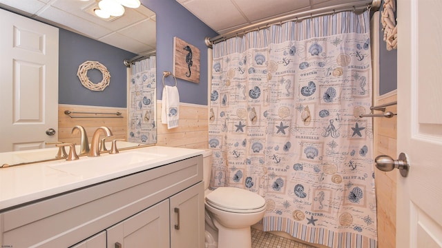 bathroom with vanity, a drop ceiling, a shower with curtain, toilet, and wood walls