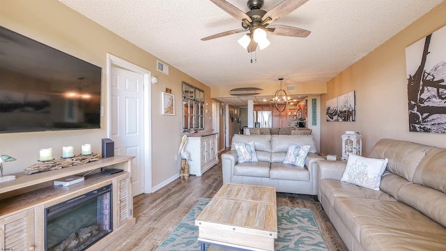 living room featuring ceiling fan with notable chandelier, a textured ceiling, and light wood-type flooring