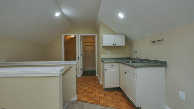 kitchen with light parquet flooring, lofted ceiling, sink, and white cabinets