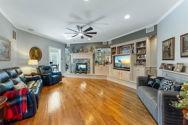 living room featuring a premium fireplace, ornamental molding, ceiling fan, and light hardwood / wood-style flooring