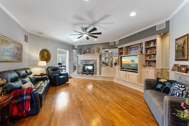 living room with ceiling fan, ornamental molding, a fireplace, and light wood-type flooring