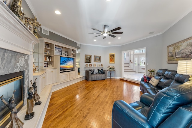 living room featuring ceiling fan, ornamental molding, a fireplace, and light wood-type flooring