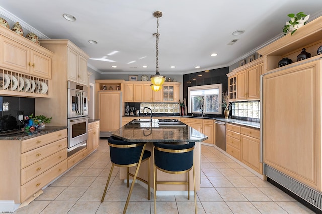 kitchen with an island with sink, appliances with stainless steel finishes, light brown cabinetry, and a kitchen bar