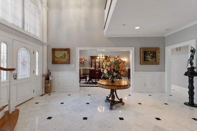 entrance foyer featuring crown molding, a wealth of natural light, a chandelier, and a towering ceiling