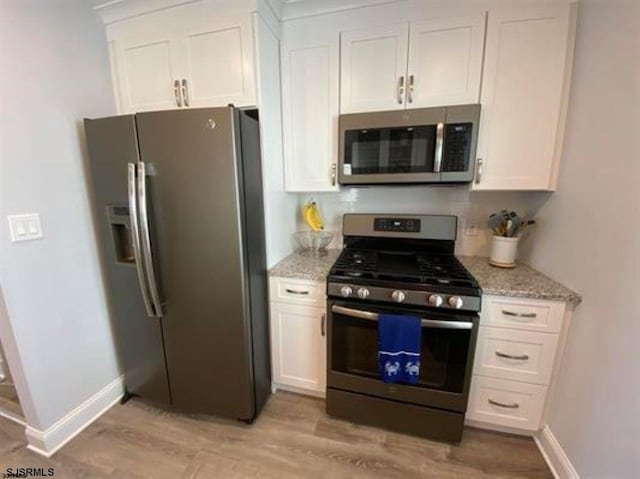 kitchen featuring light stone countertops, light hardwood / wood-style floors, white cabinets, and appliances with stainless steel finishes