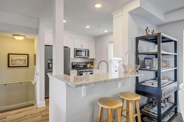 kitchen featuring a breakfast bar area, white cabinetry, light stone counters, appliances with stainless steel finishes, and kitchen peninsula