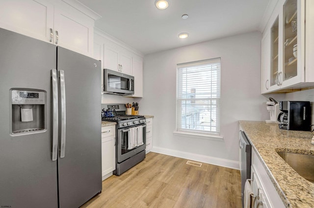 kitchen with white cabinetry, light stone counters, light wood-type flooring, and appliances with stainless steel finishes