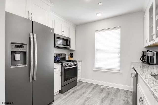 kitchen featuring a healthy amount of sunlight, appliances with stainless steel finishes, light stone countertops, and white cabinets