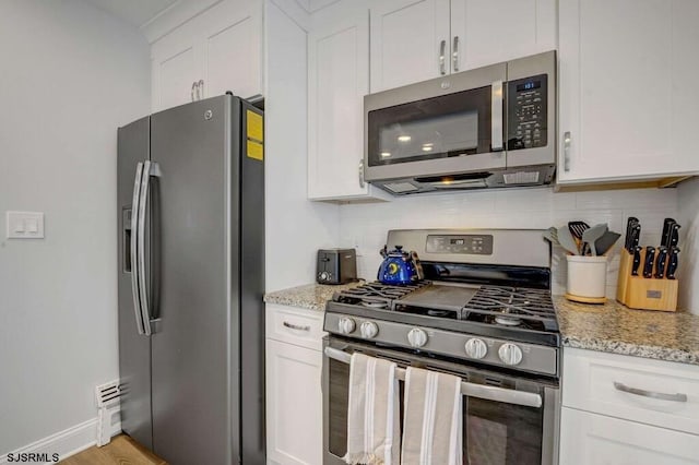 kitchen featuring stainless steel appliances, white cabinetry, light stone countertops, and backsplash