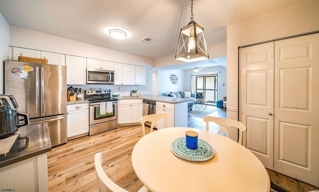 kitchen featuring white cabinetry, hanging light fixtures, light wood-type flooring, appliances with stainless steel finishes, and decorative backsplash