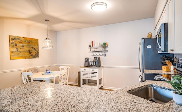 kitchen with pendant lighting, stainless steel appliances, light stone countertops, and white cabinets