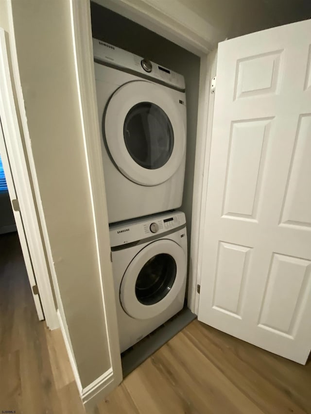 clothes washing area with stacked washer / drying machine and wood-type flooring