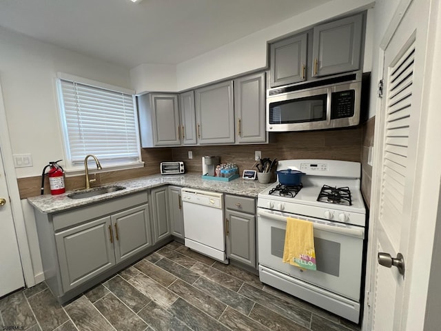 kitchen with sink, gray cabinetry, light stone counters, tasteful backsplash, and white appliances