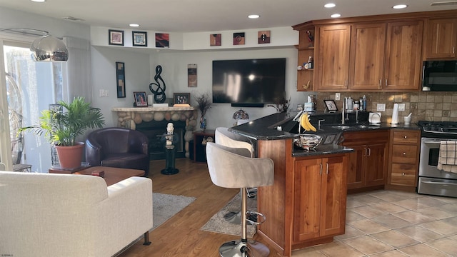 kitchen with sink, stainless steel gas stove, dark stone countertops, decorative backsplash, and kitchen peninsula