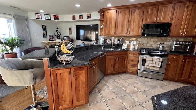 kitchen featuring a kitchen bar, kitchen peninsula, dark stone counters, and appliances with stainless steel finishes