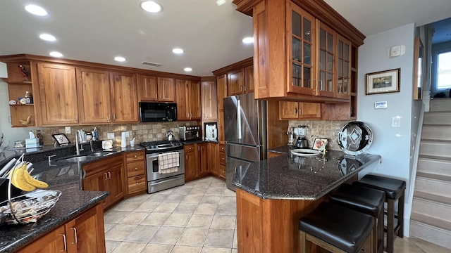 kitchen with sink, light tile patterned floors, dark stone countertops, kitchen peninsula, and stainless steel appliances