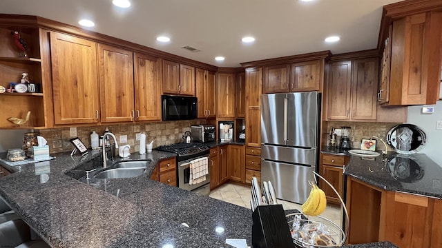 kitchen with appliances with stainless steel finishes, sink, dark stone counters, light tile patterned floors, and kitchen peninsula