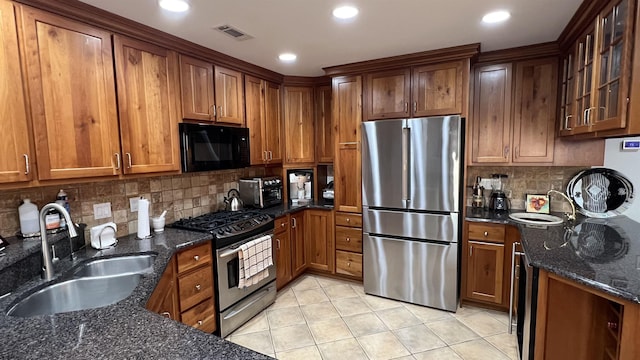 kitchen featuring sink, light tile patterned floors, dark stone counters, and appliances with stainless steel finishes