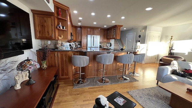 kitchen featuring stainless steel fridge, a breakfast bar area, backsplash, kitchen peninsula, and light wood-type flooring