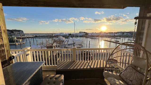 balcony at dusk featuring a water view and a dock