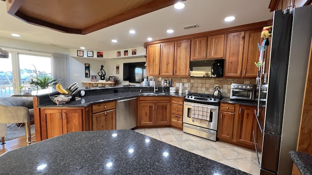 kitchen featuring dark stone countertops, sink, stainless steel appliances, and kitchen peninsula