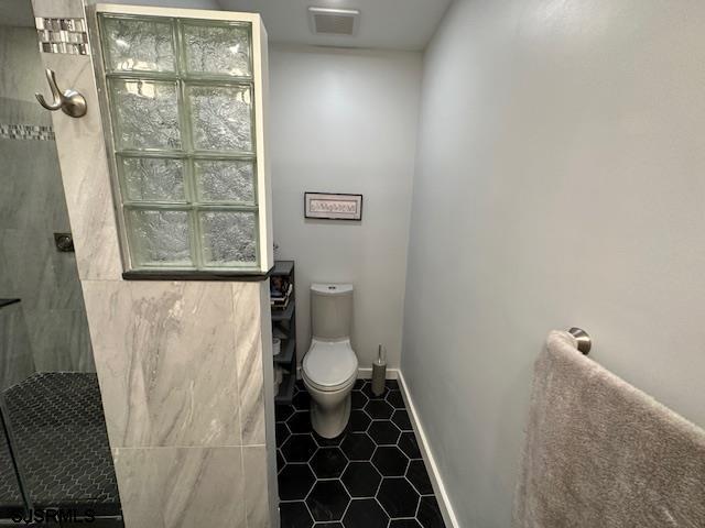 bathroom featuring toilet, tile patterned flooring, and a tile shower