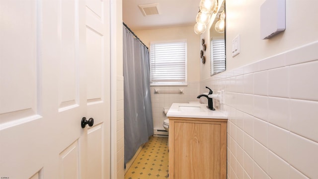 bathroom with vanity, toilet, tile walls, and a baseboard heating unit