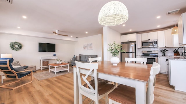 dining space featuring sink, ceiling fan with notable chandelier, and light wood-type flooring