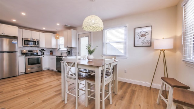 kitchen with white cabinetry, appliances with stainless steel finishes, hanging light fixtures, and backsplash