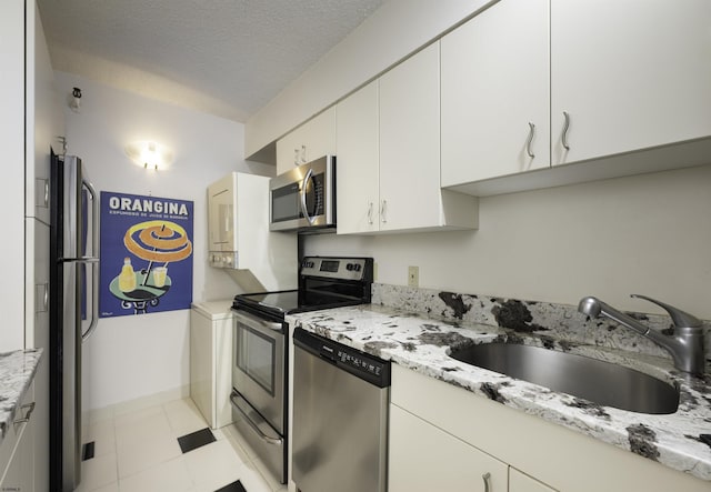 kitchen with white cabinetry, sink, light stone counters, stainless steel appliances, and a textured ceiling