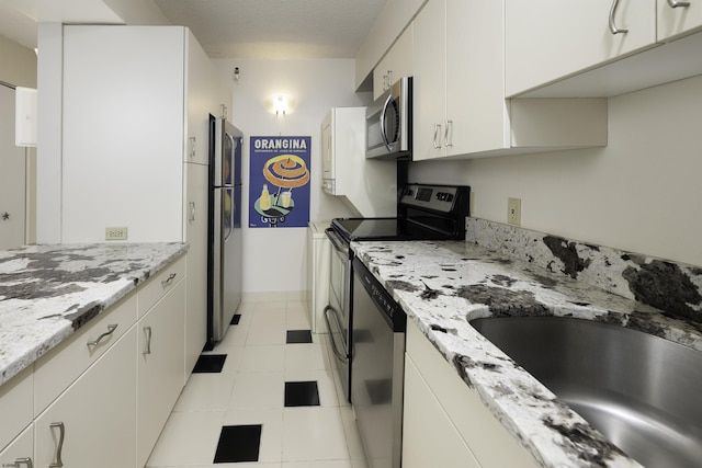 kitchen with sink, white cabinetry, stainless steel appliances, light stone counters, and light tile patterned flooring