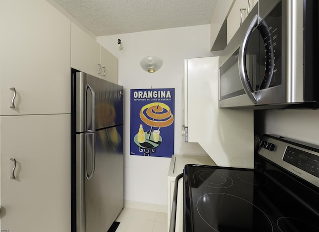 kitchen with appliances with stainless steel finishes, light tile patterned floors, white cabinets, and a textured ceiling