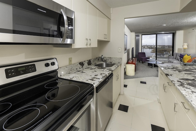 kitchen featuring white cabinetry, sink, light stone counters, stainless steel appliances, and a textured ceiling