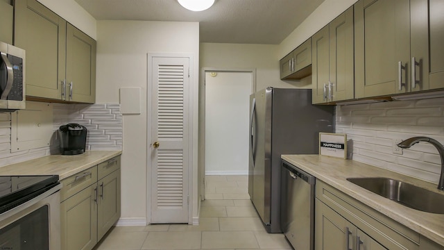 kitchen with sink, green cabinets, appliances with stainless steel finishes, light tile patterned flooring, and decorative backsplash