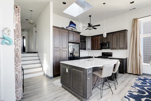 kitchen with a skylight, dark brown cabinets, pendant lighting, stainless steel appliances, and a kitchen island with sink