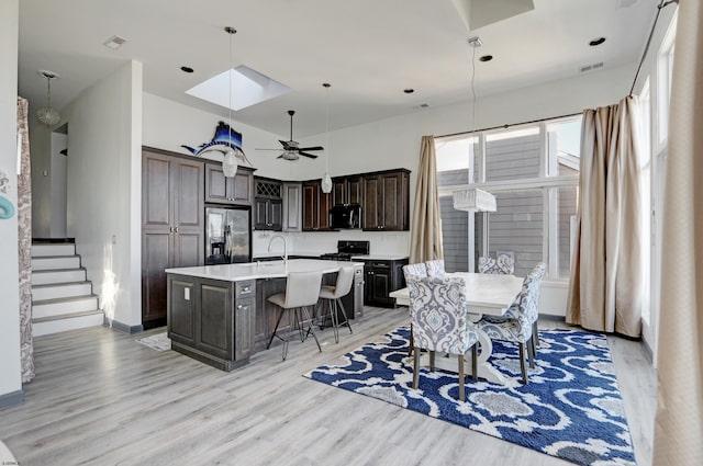 kitchen featuring pendant lighting, black appliances, light hardwood / wood-style floors, dark brown cabinetry, and a center island with sink