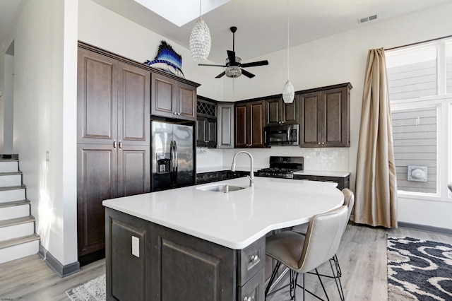 kitchen featuring stainless steel appliances, dark brown cabinets, sink, and a kitchen island with sink