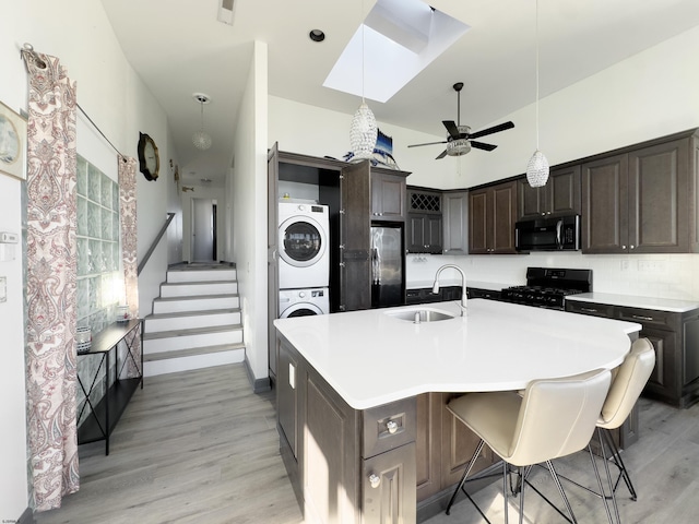 kitchen featuring stacked washer and clothes dryer, a breakfast bar, sink, black range oven, and a kitchen island with sink